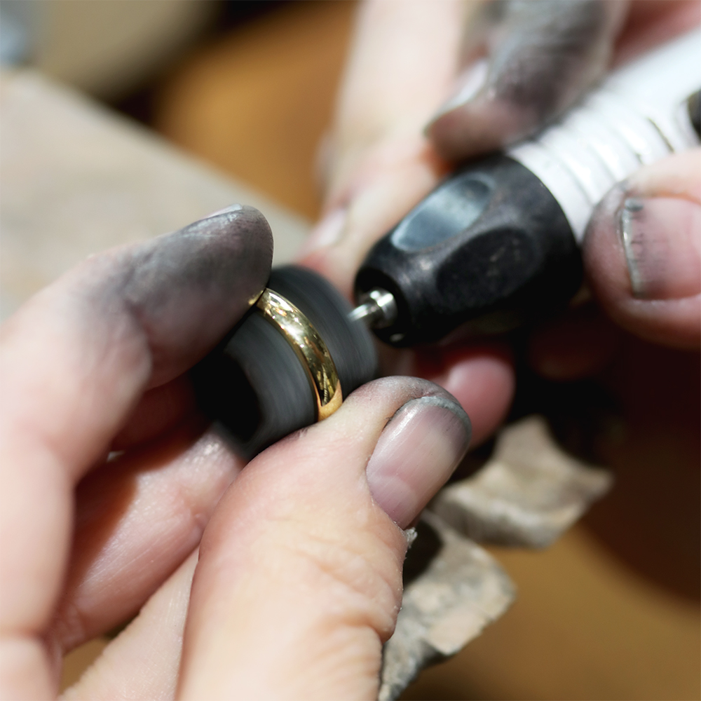 Jeweler's hands polishing a solid gold ring with a rotary tool at the workbench
