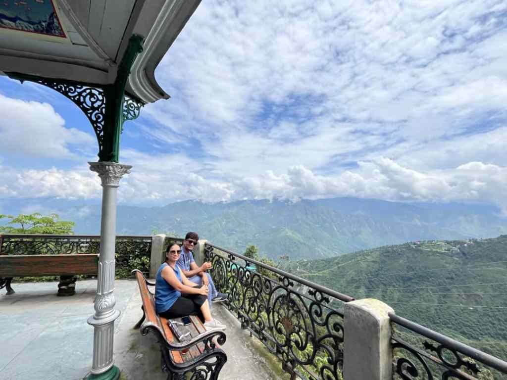 A couple seated at a mountain viewpoint overlooking lush green hills
