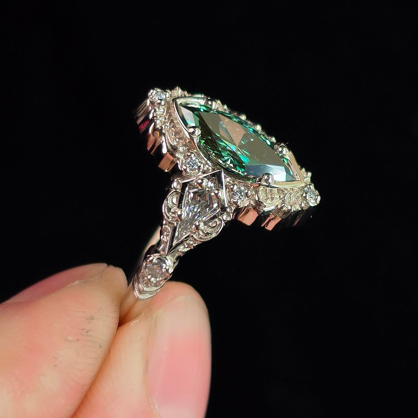 Hand holding an ornate gold ring with a marquise green gemstone