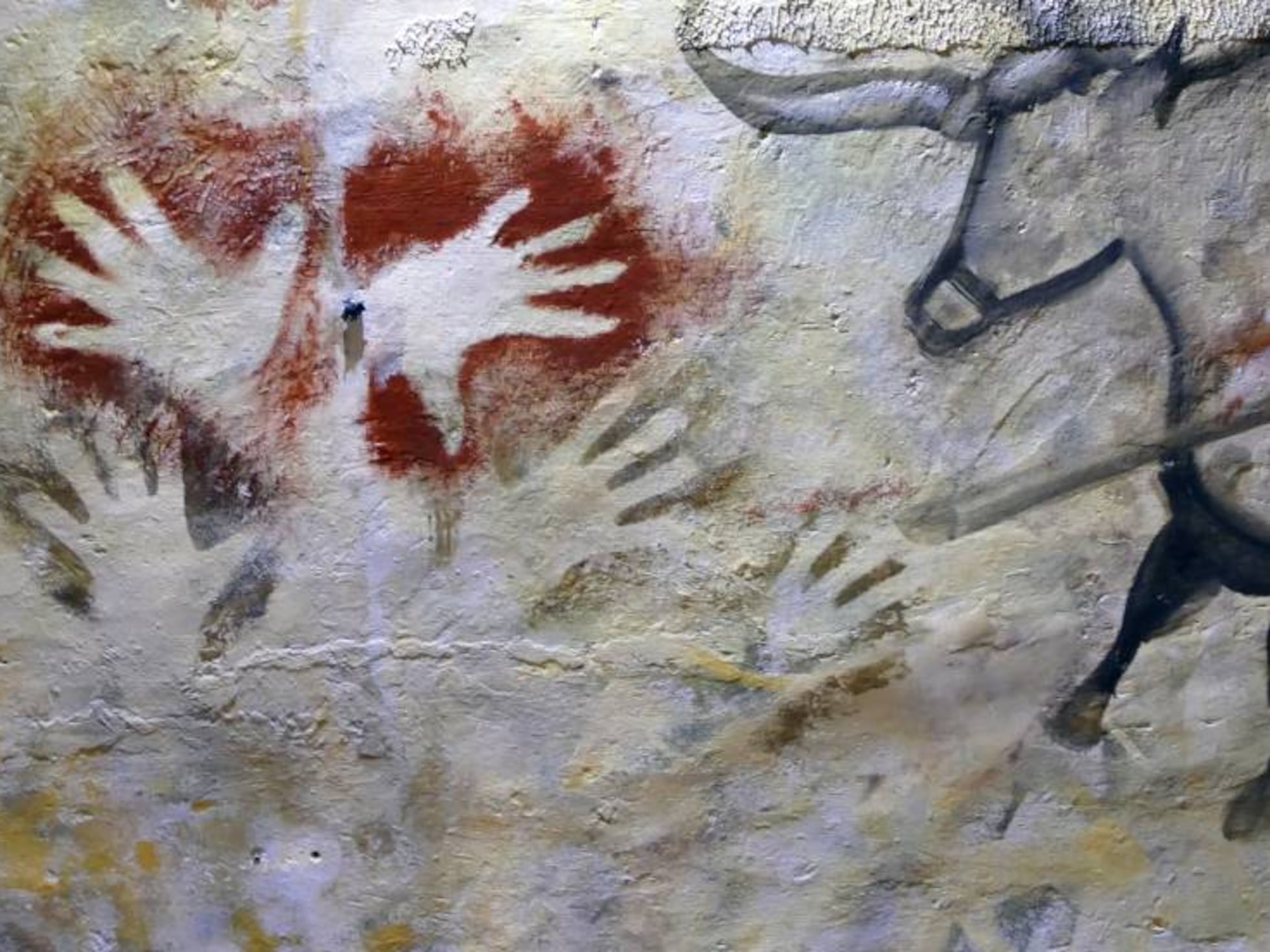 Hand stencils blown in red pigment beside an animal figure — Paleolithic cave art.