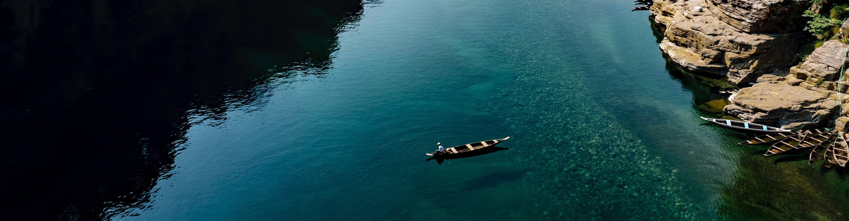 Aerial panorama of a lone boat on the emerald Umngot river between forested cliffs