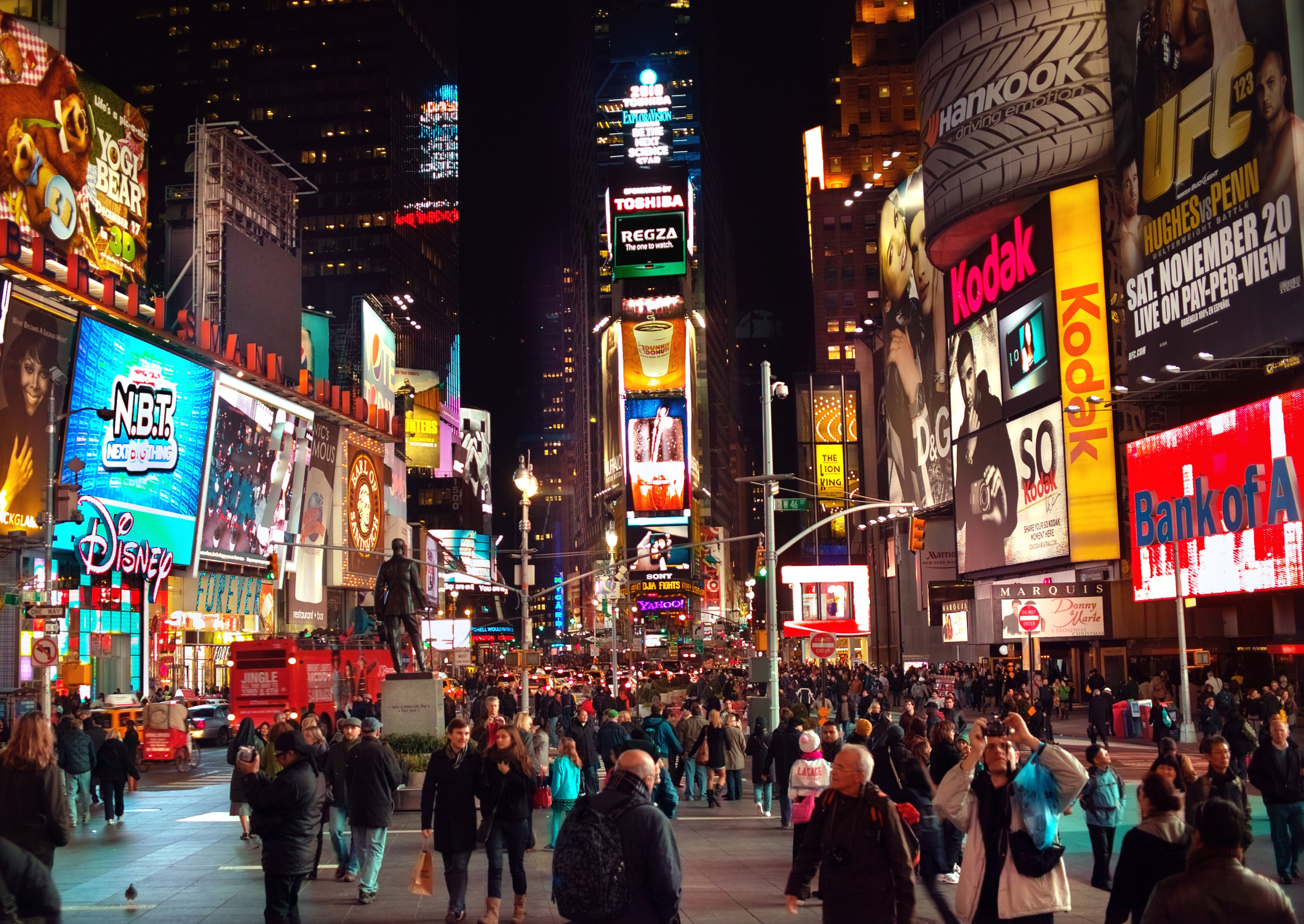 Crowds passing festive advertising screens in a big city at night, where the holiday ad wars play out every December