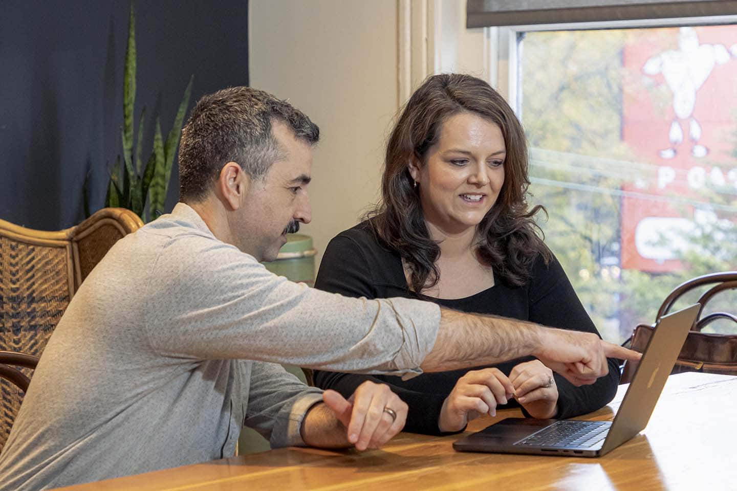 Two marketers reviewing AI-generated ad creative on a laptop together, testing the best AI ad generators side by side