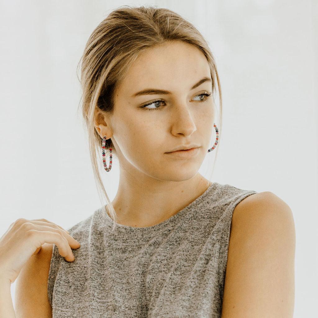 Woman with blonde updo wearing beaded gold hoop earrings and a grey sleeveless top