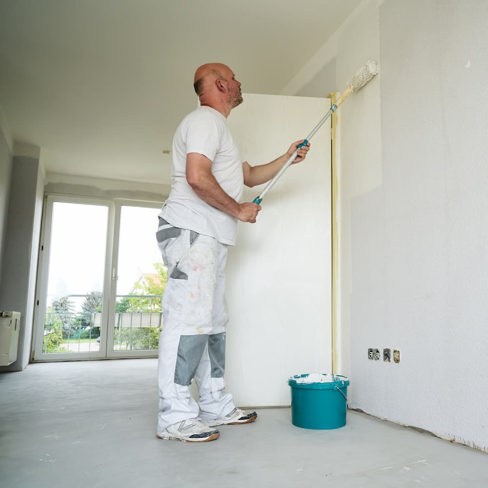 Handwerker streicht eine Wand in einer hellen, leeren Wohnung