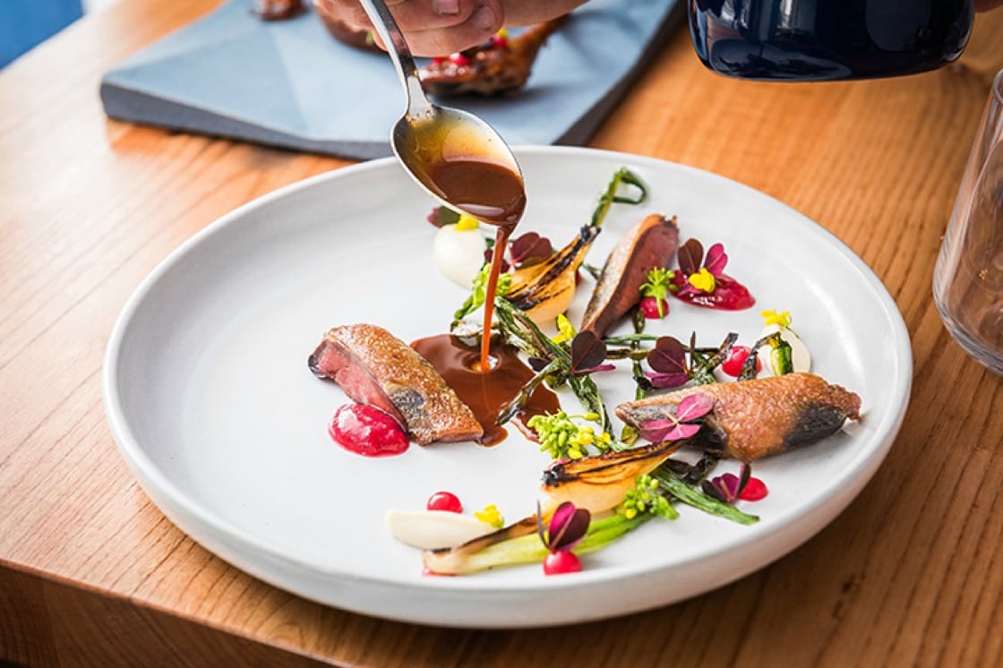 A gourmet dish being finished with a sauce pour