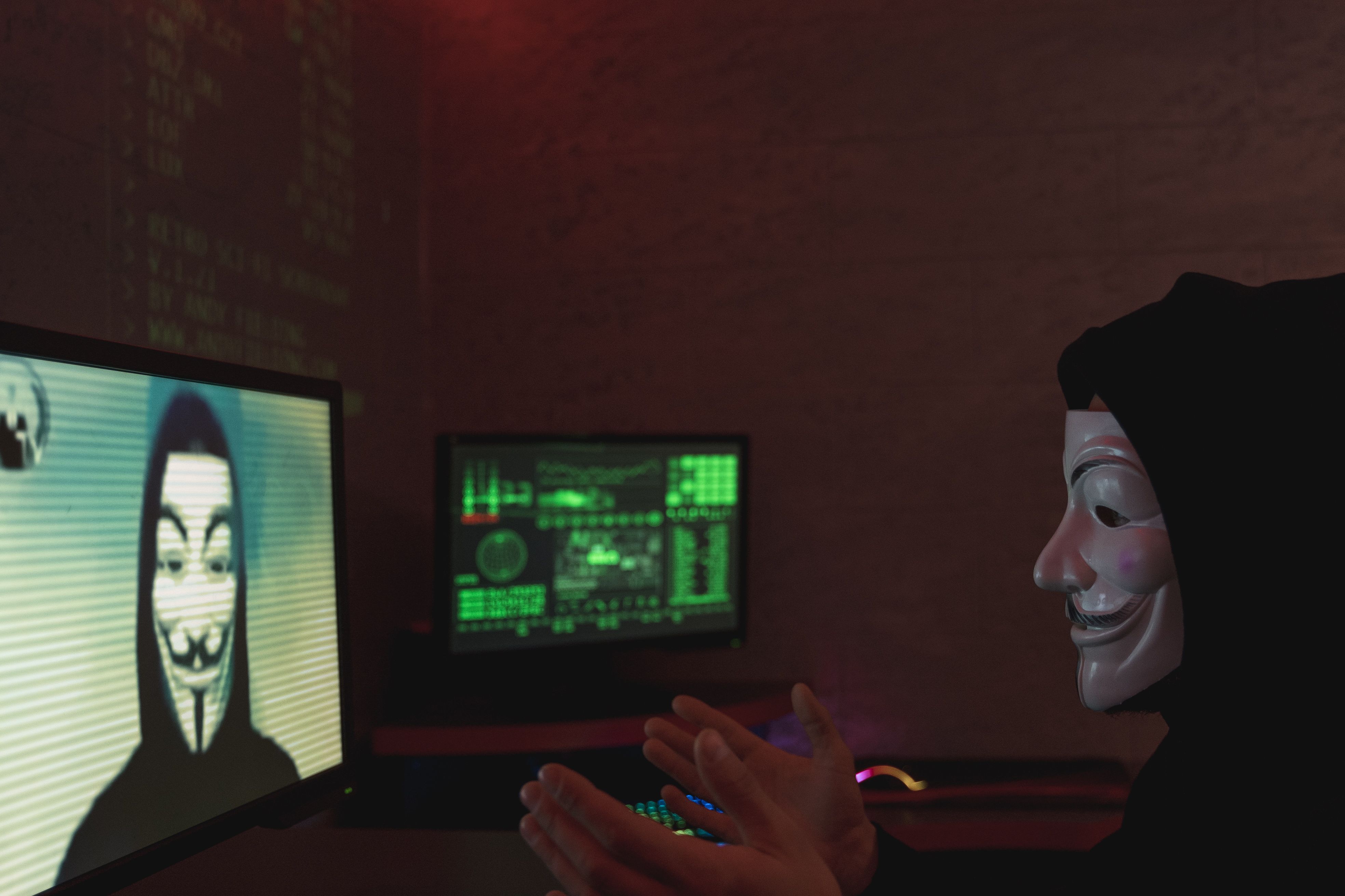 Anonymous masks in front of glowing monitors, a visual shorthand for online fraud operations