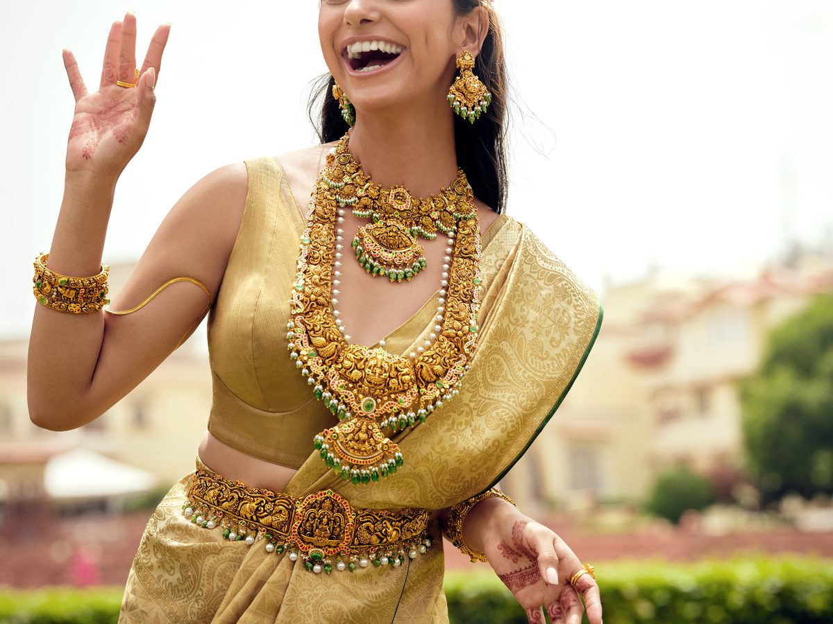 Joyful Indian bride in gold silk saree wearing elaborate traditional gold jewellery