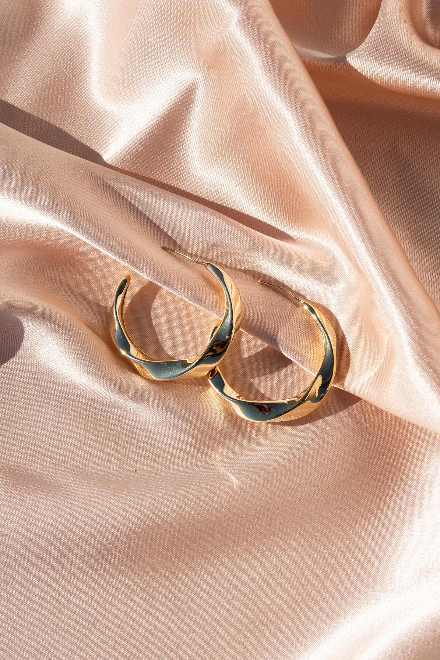 Sasha twisted gold hoop earrings on draped blush satin