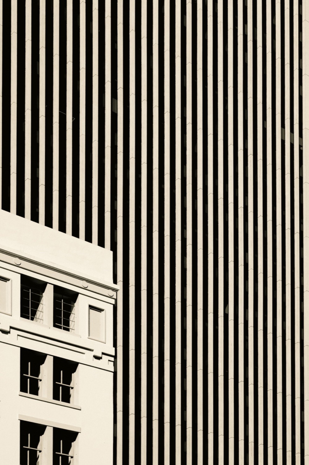 Black and white photograph of a striped skyscraper facade beside a classic building corner